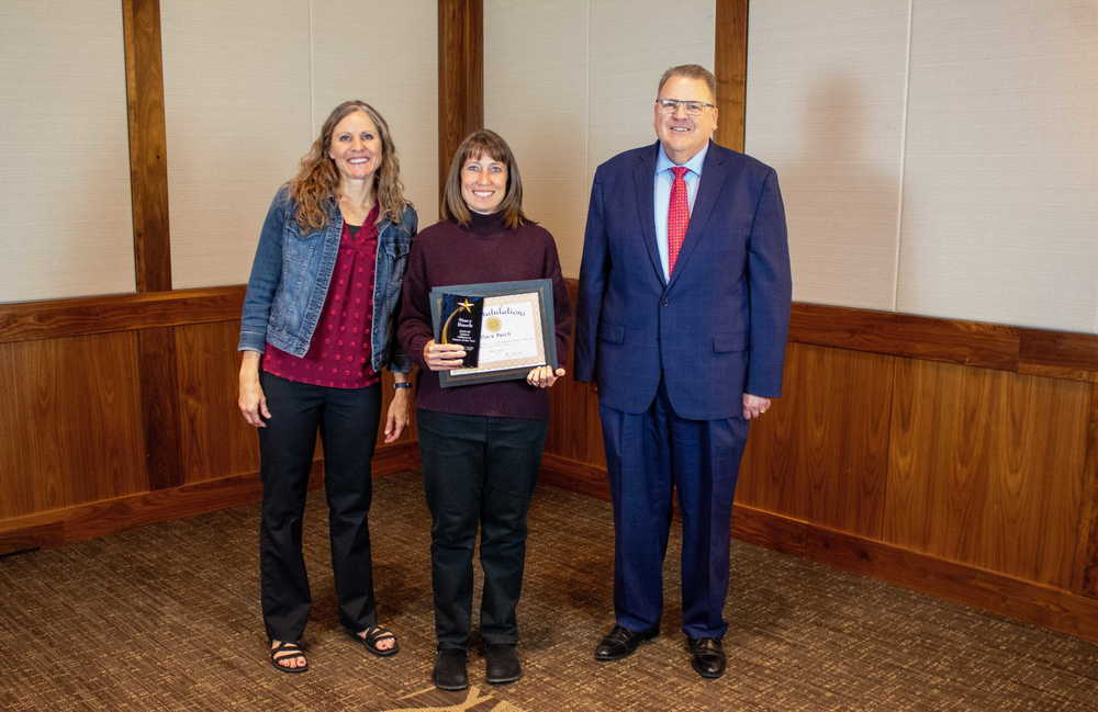 Woman in black pants and purple sweater standing in the middle of a main in a suit and a woman in slacks and a jean jacket