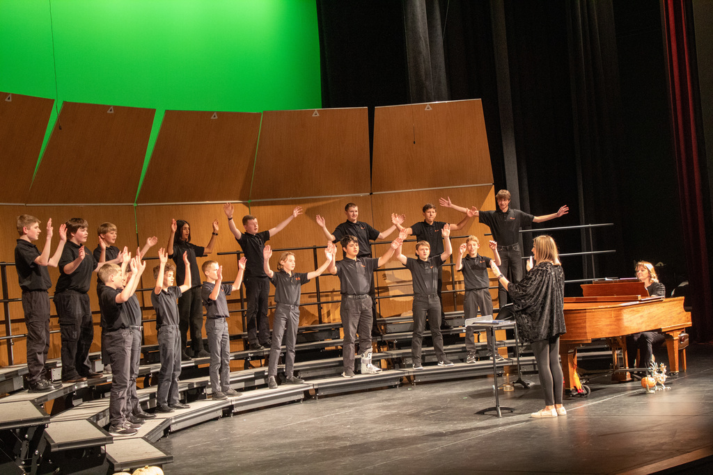 Students standing on three row risers, singing to audience.