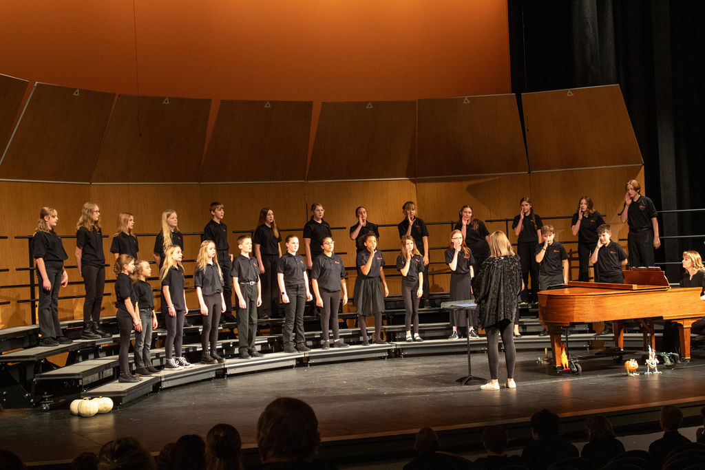 Students standing on three row risers, singing to audience.