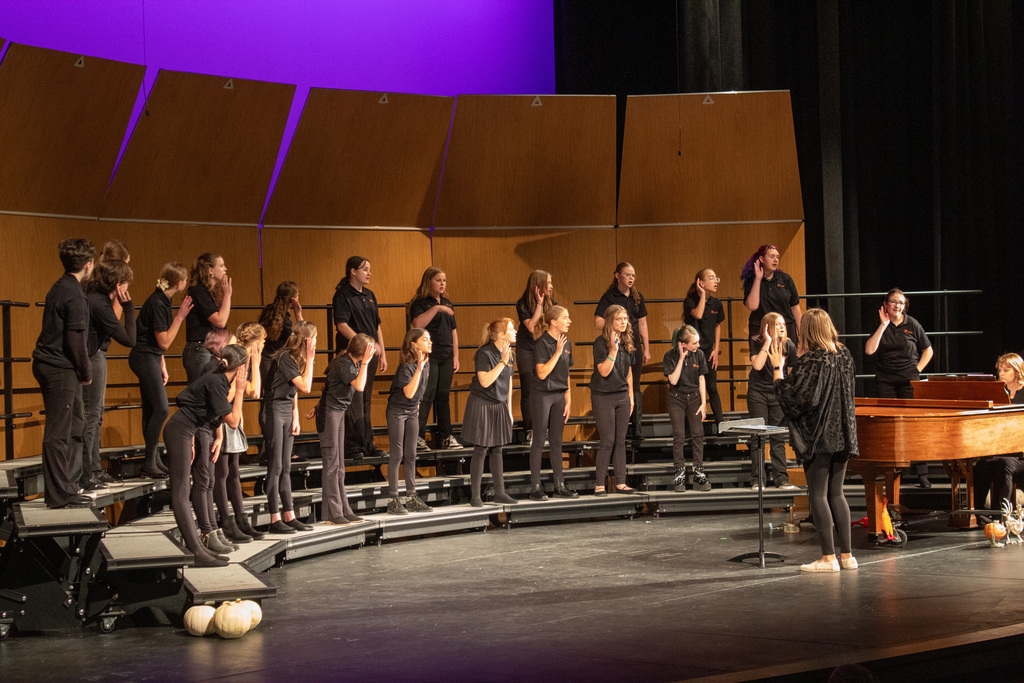 Students standing on three row risers, singing to audience.
