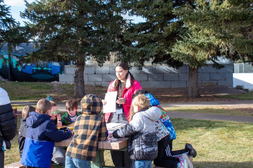 Students sitting at picnic table in park being taught by teacher