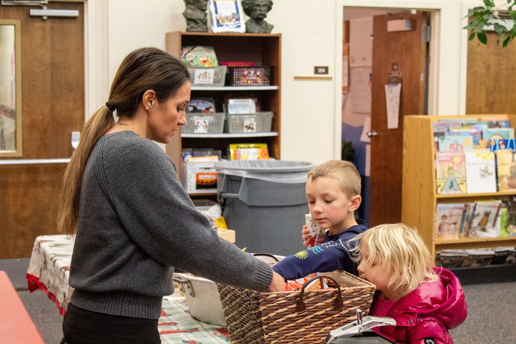 Children grabbing breakfast from a teacher holding a basket