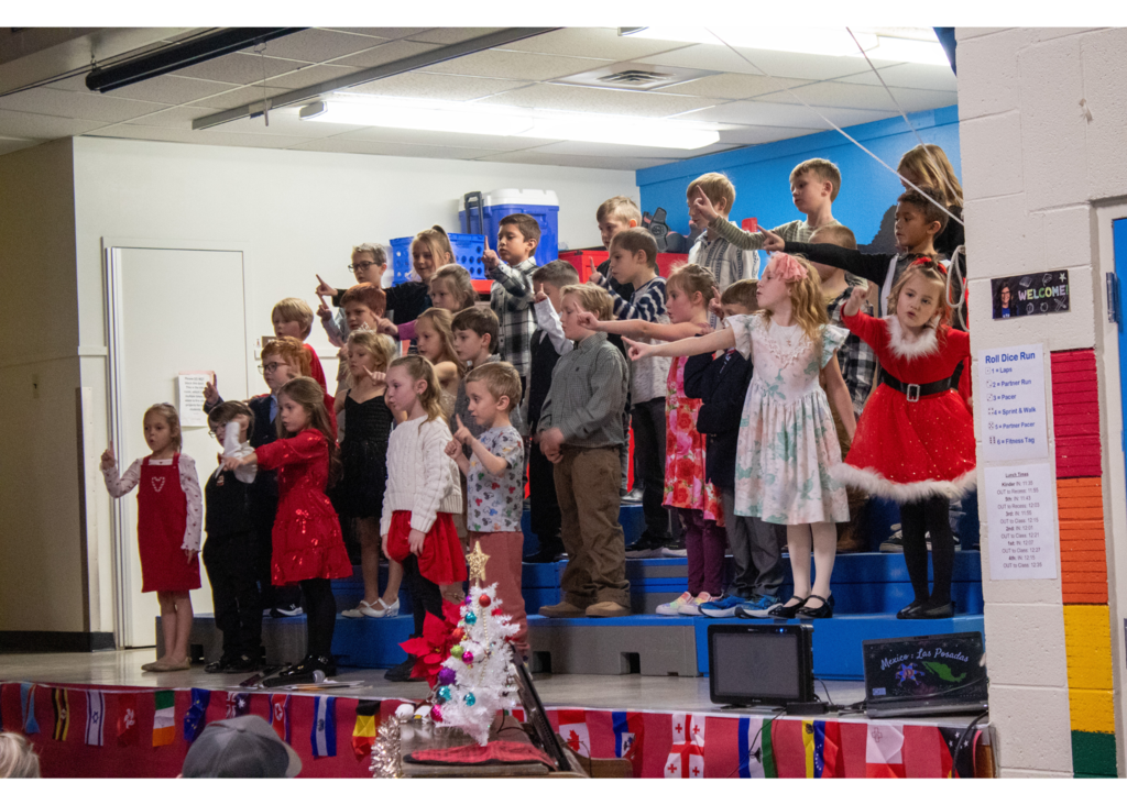 students standing on stage singing for a gym full of parents and staff