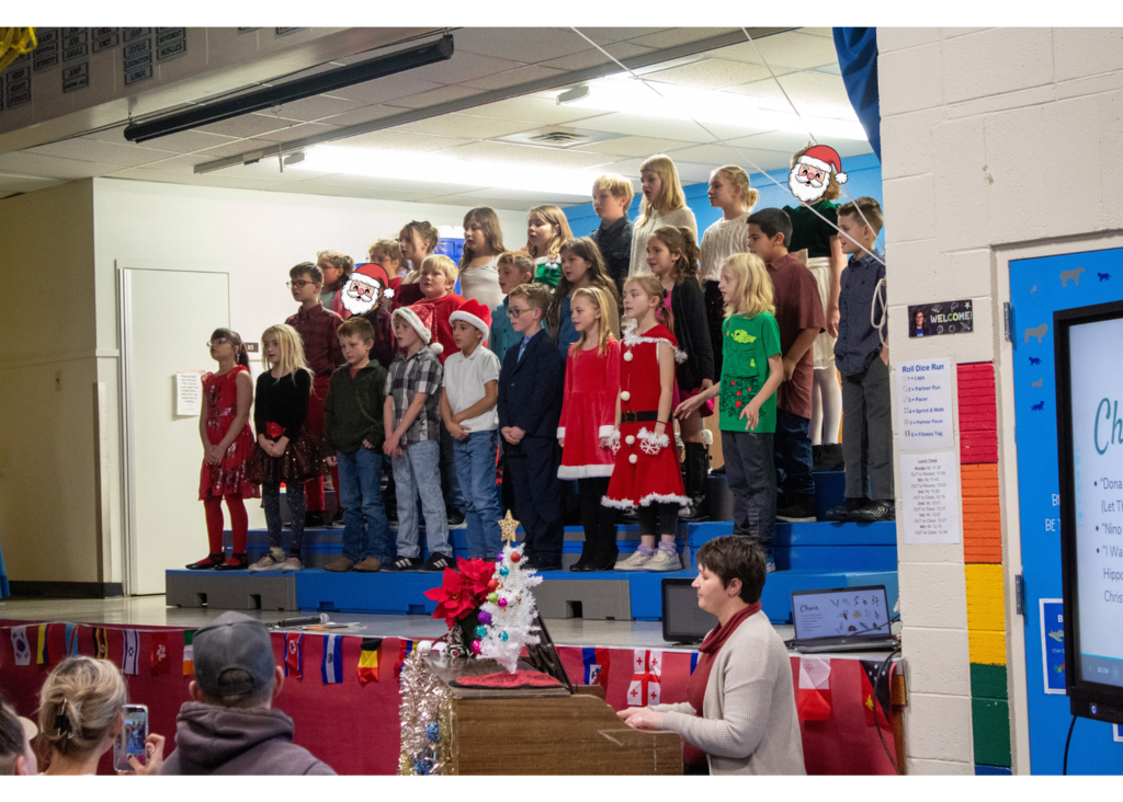 students standing on stage singing for a gym full of parents and staff