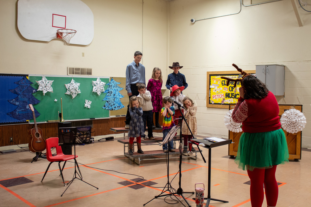 children on risers singing in front of a teacher conducting the music