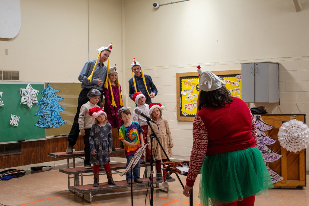 children on risers singing in front of a teacher conducting the music