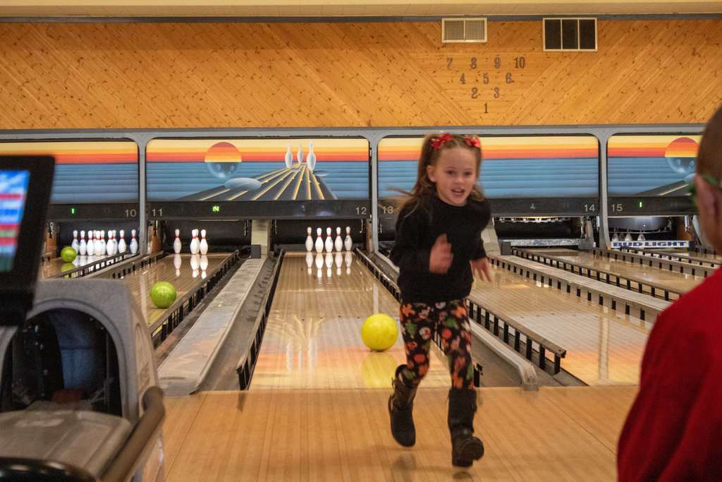 young girl running back to friends after bowling