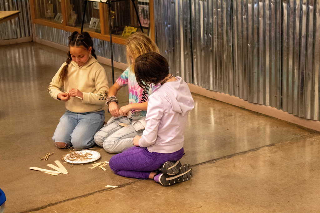 Three young girls sitting on the floor with a pile of wood shavings