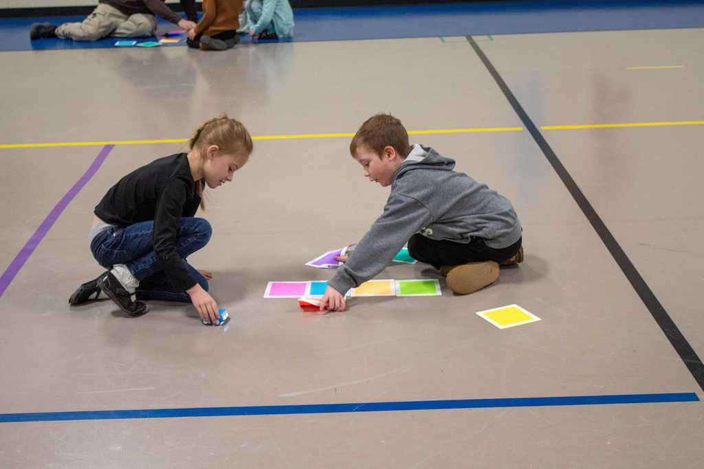 young girl and boy placing paper colored mats to drive toy car on