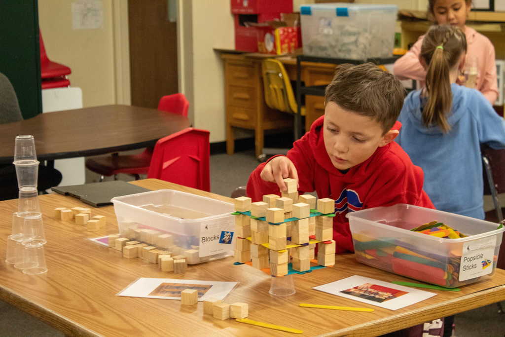Young boy with brown hair stacking small blocks and plastic cups
