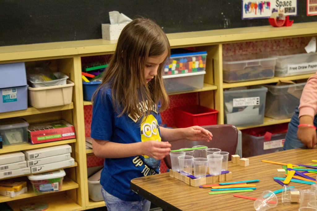 Young girl with brown hair stacking small blocks and plastic cups