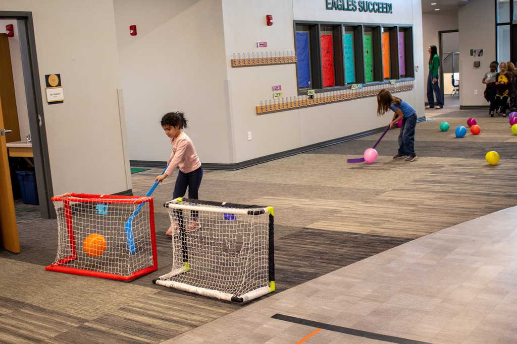 two students oushing balloons into a net with hockey sticks