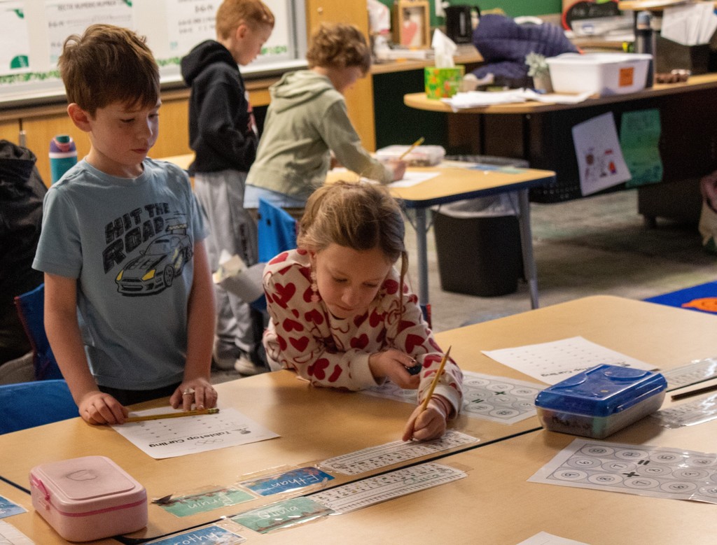 Two young students completing a math worksheet together at desk