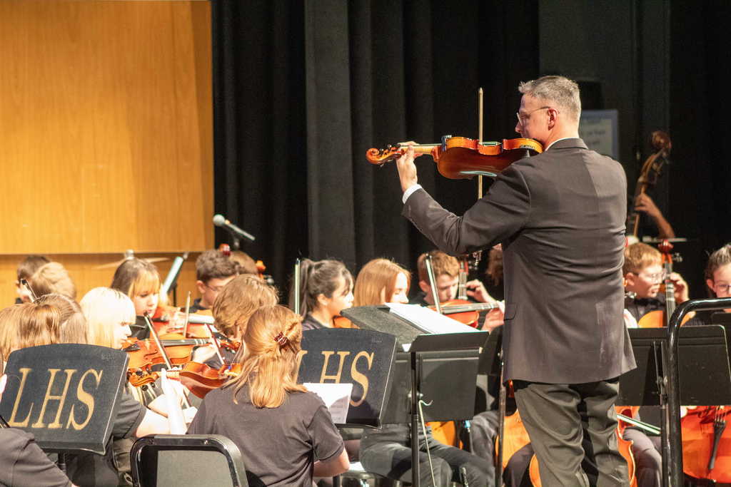 Students standing playing orchestra instruments on the stage