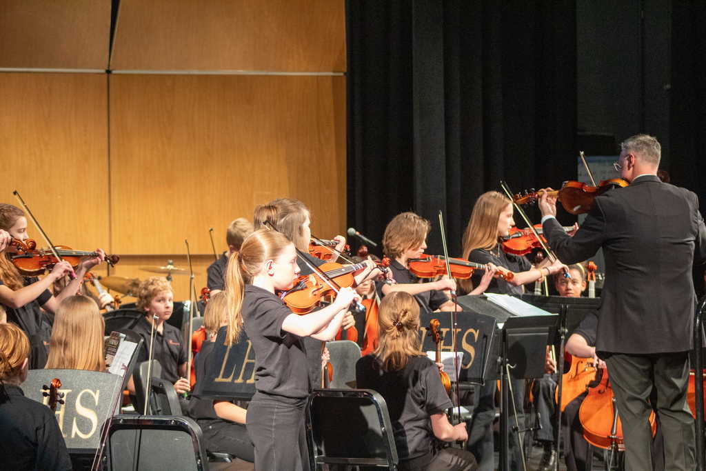 Students standing playing orchestra instruments on the stage