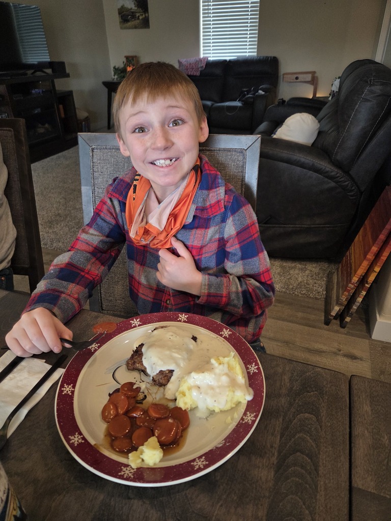 young boy smiling with a plate of food set in front of him