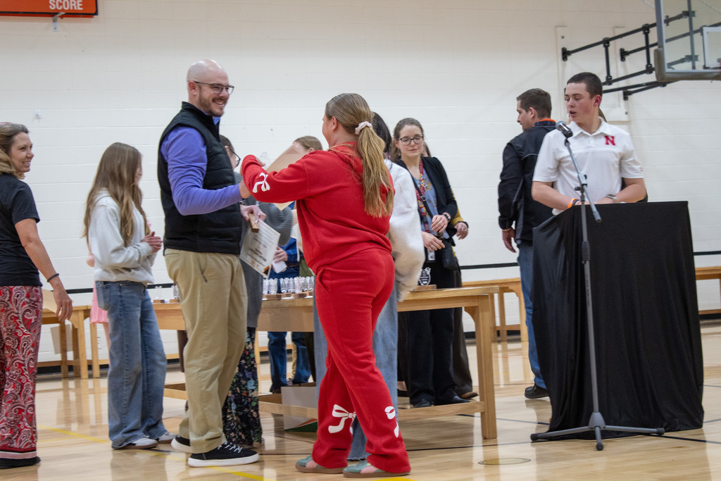 Student dressed in red suit grabbing award from teacher