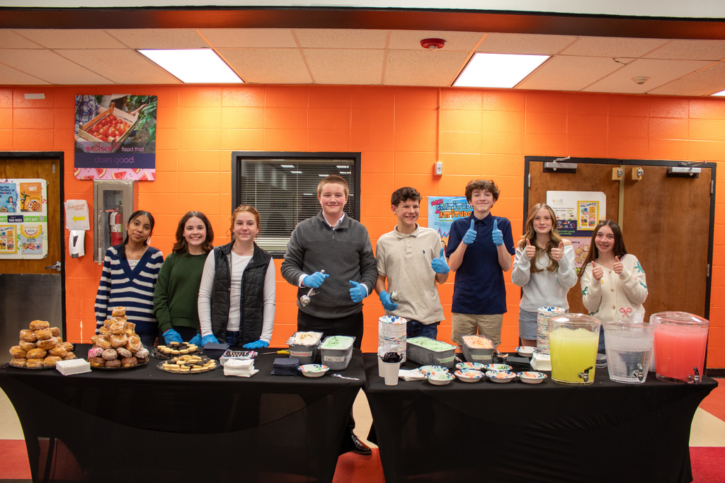 Students posing behind table of baked goods