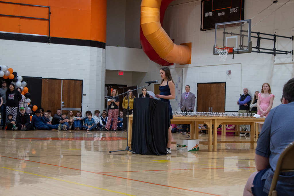 young female student with brown hair in dark dress talking at a podium