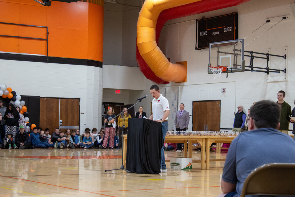 young male student with brown hair in white shirt talking at a podium