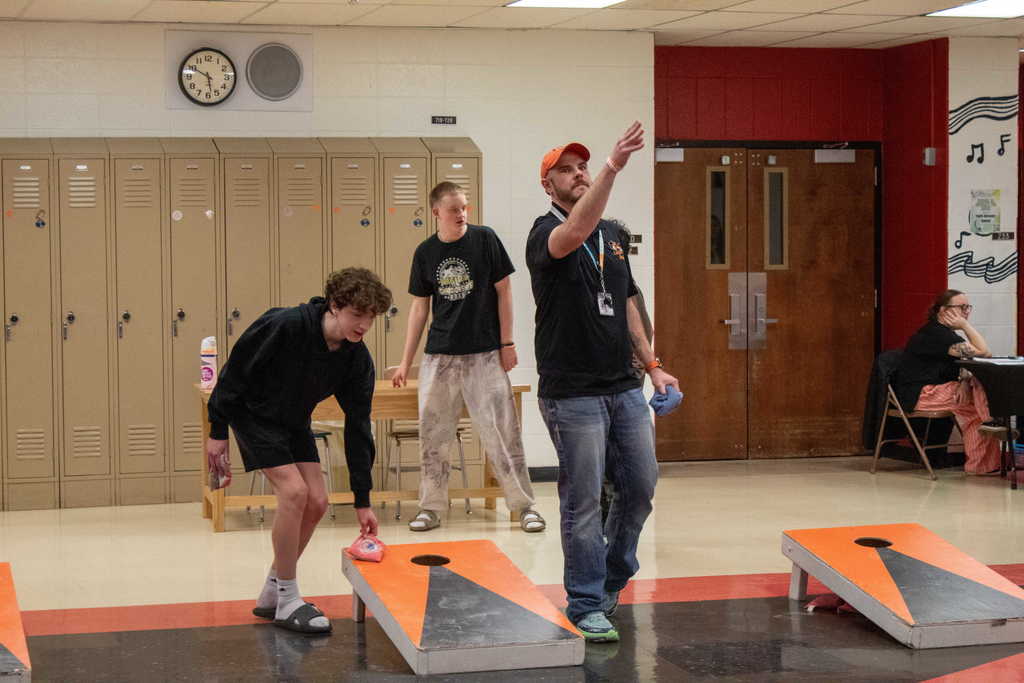 3 men dressed in black t-hisrts playing cornhole
