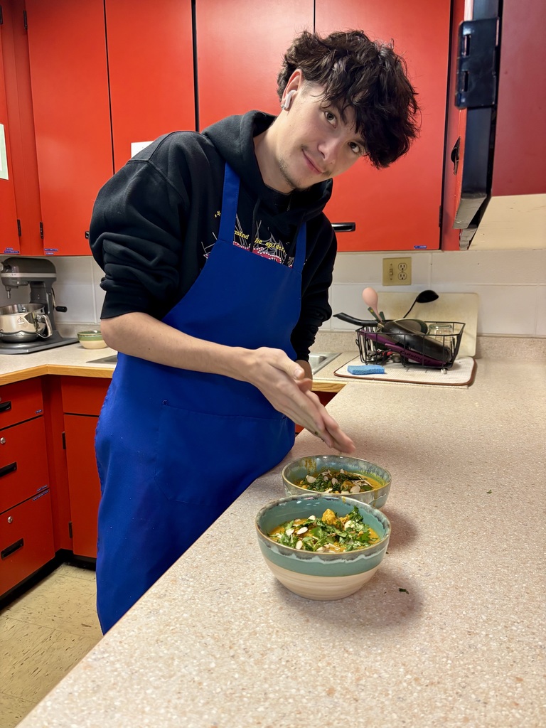 Male student pointing to two bowls of soup that he prepared