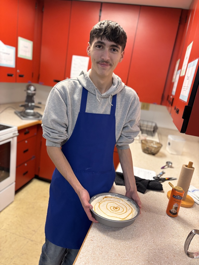 Male student in a blue appron holding a pie