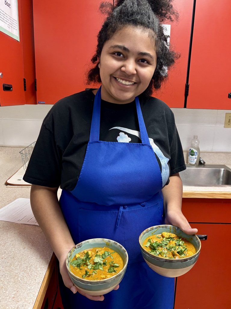 Female student in blue apron holding two bowls of soup