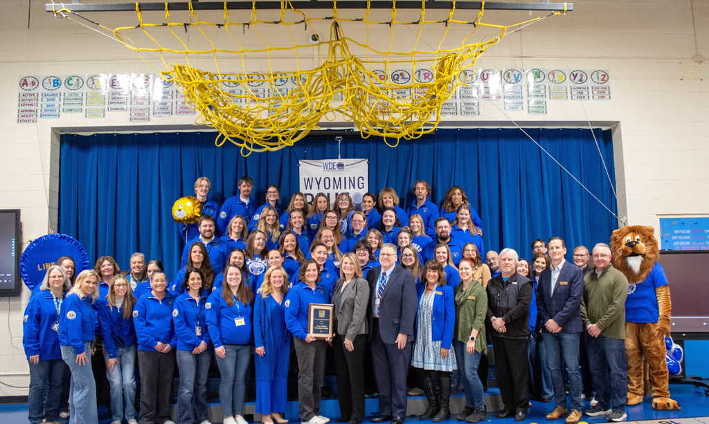 Group of teachers and guest dressed in blue shirts standing on risers