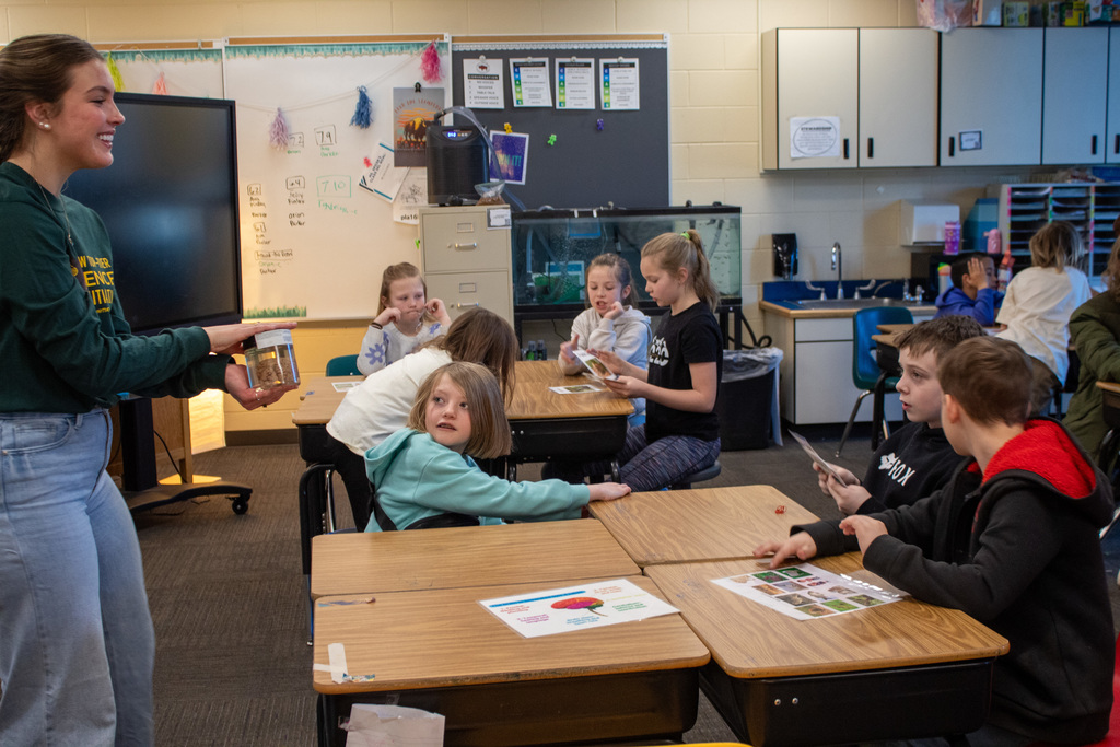 You women holding up a jar for students to see