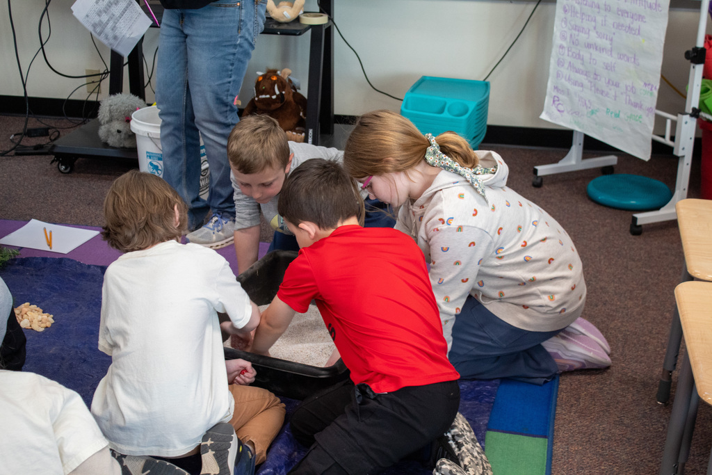 Students sitting around a black bucket full of sand