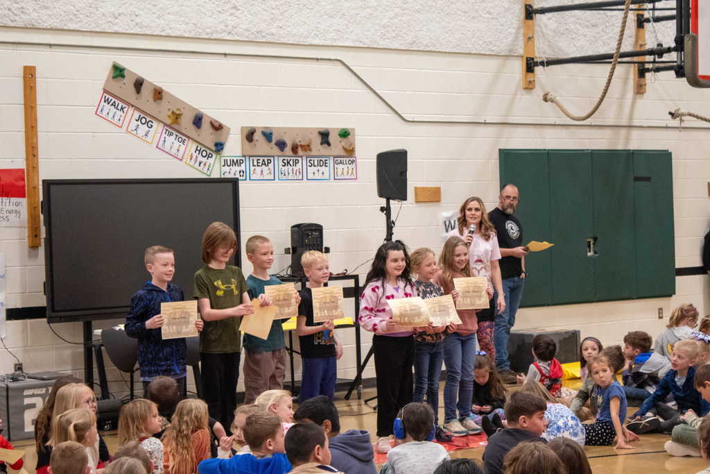 Group of elementary students standing in front of gym holding their certificates