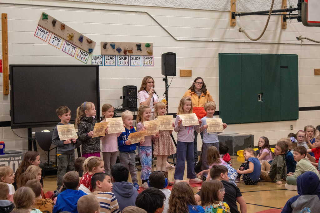 Group of elementary students standing in front of gym holding their certificates