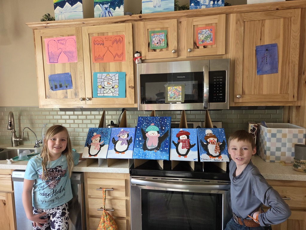 Young girl and boy standing next to row of penguin paintings