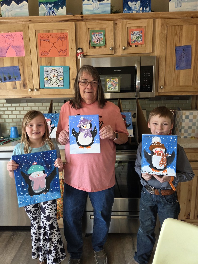 Young girl and boy and teacher holding up paintings of penguins