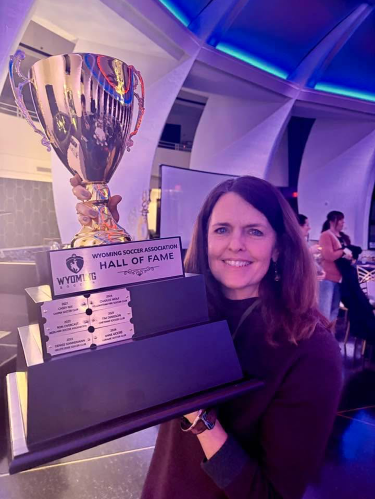 Woman with  brown hair holding large trophy title Wyoming Soccer Association Hall of Fame