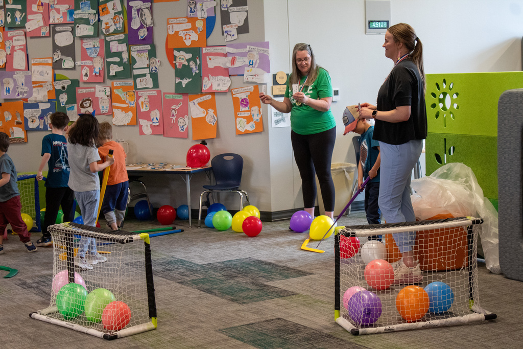 Students pusing hockey sticks to hit baloons into a net
