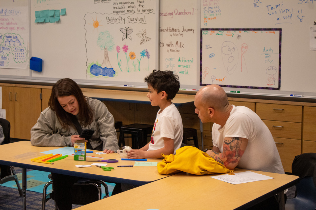 Young male student sitting at desk with his mother and father