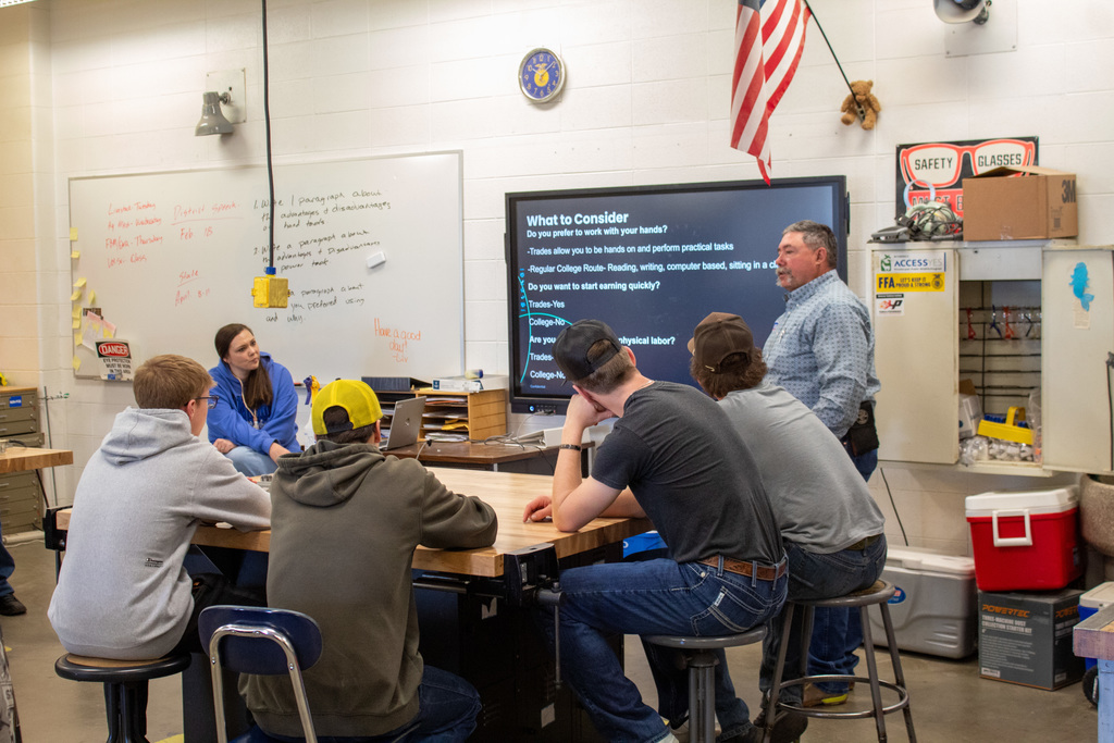 Four young men sitting listening to a a man giving a presentation
