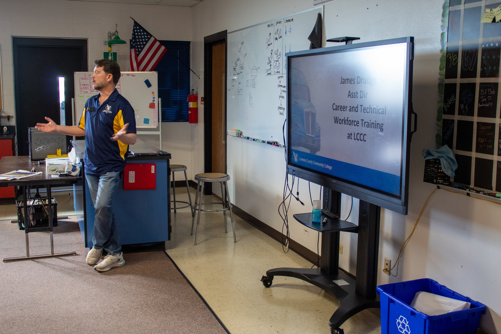 Man in blue shirt and jeans standing next to a powerpoint presentation displayed on a whiteboard
