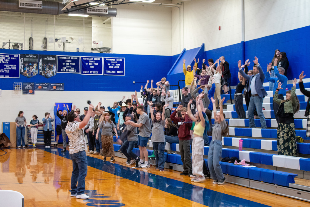 Man standing in front of stands raising his hands alongside students