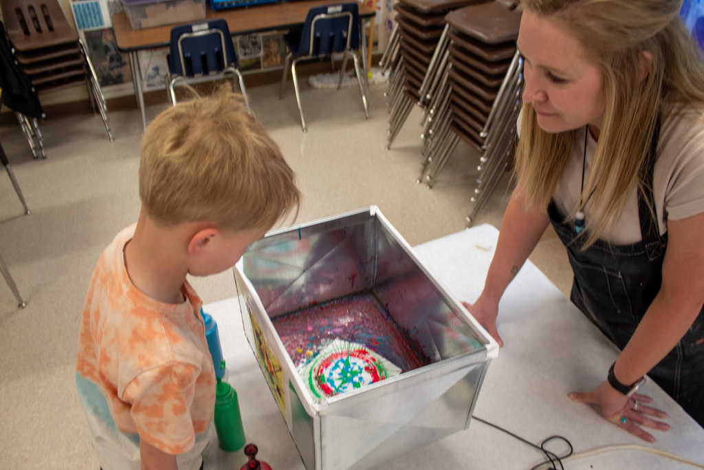Young boy working with teacher to make spin art