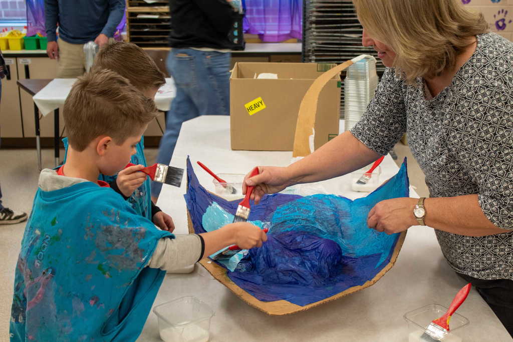 Two young boyws painting with teacher