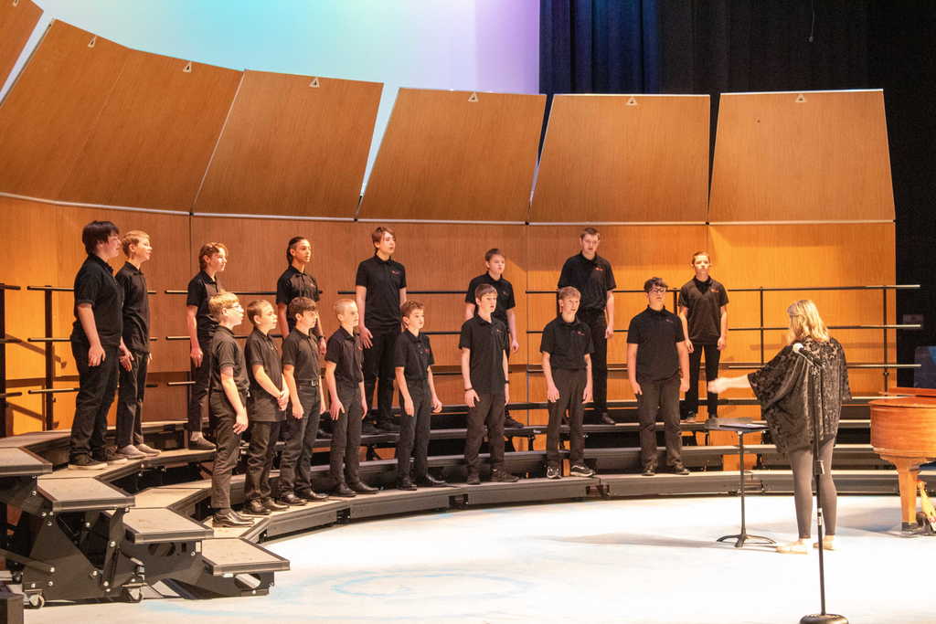 Student choir singing on stage with a teacher director