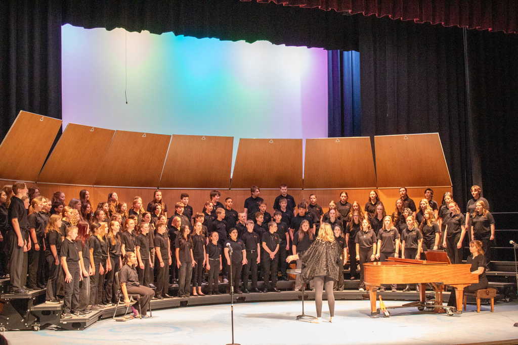 Student choir singing on stage with a teacher director