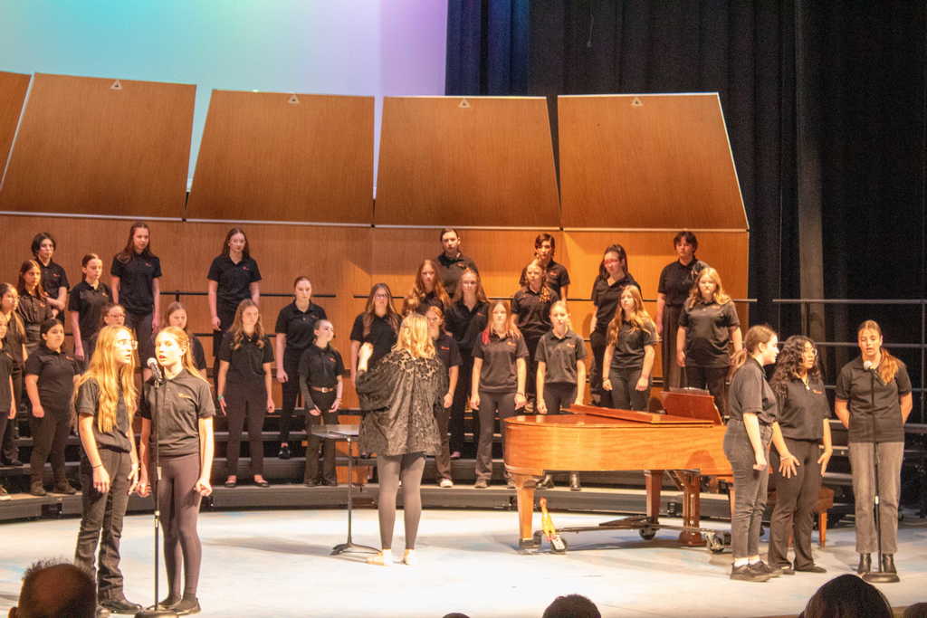 Student choir singing on stage with a teacher director