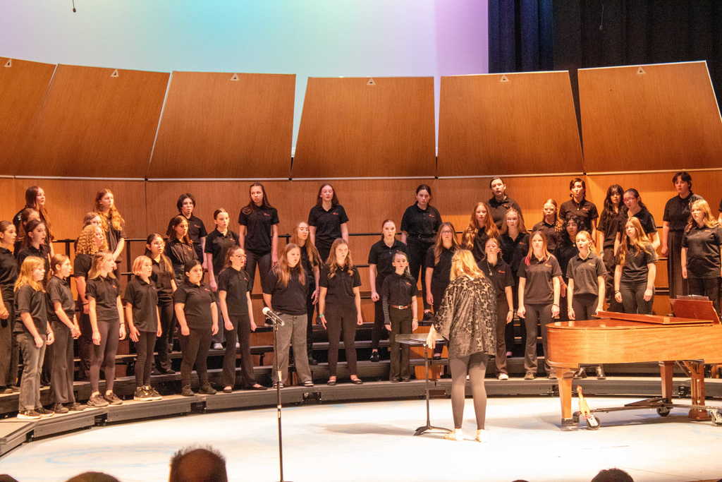 Student choir singing on stage with a teacher director