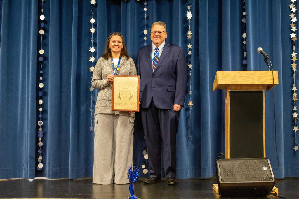women with brown hair holding a plaque standing next to a man in a blue sute