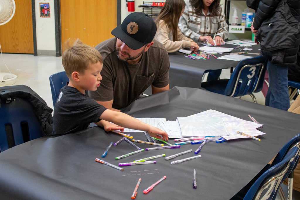 Young boy sitting with father while he writes a note