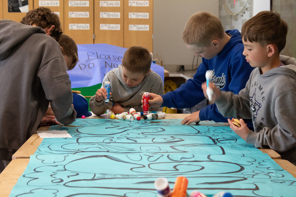 Students coloring on a large blue coloring sheet with markers